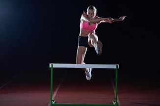 Determined young woman athlete jumping over a hurdles