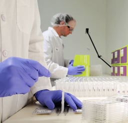 Men in white lab coasts, gloves and hair nets assemble Mitra Clamshell Devices