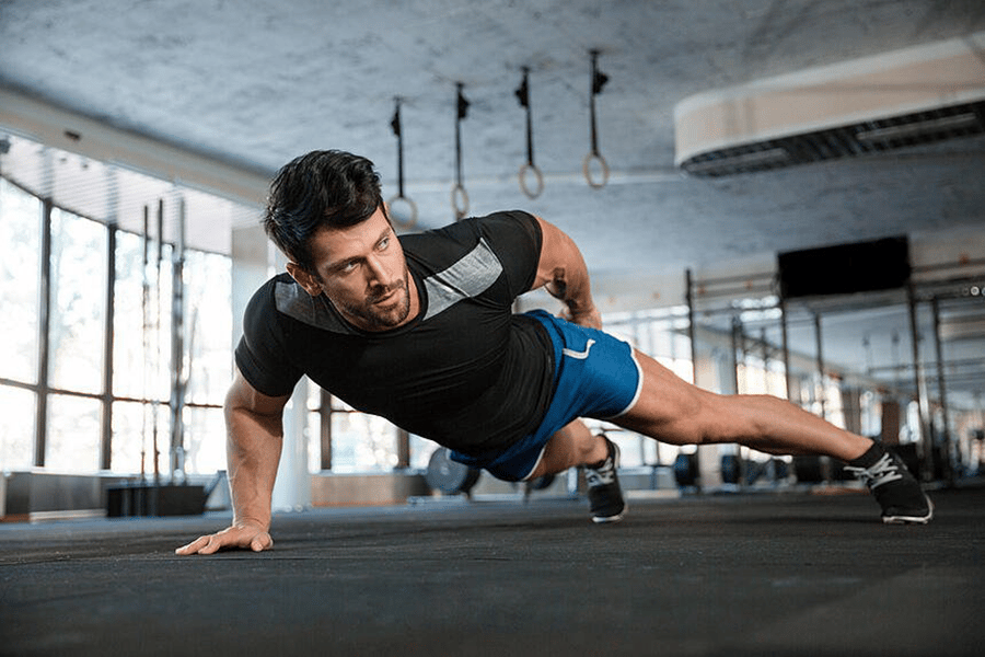 A fit man in a gym does a one-handed push up.