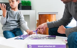 A young male pediatric patient looks at his cell phone while his father collects a blood sample from home. 