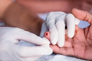 A pair of gloved hands take a capillary blood sample from a finger