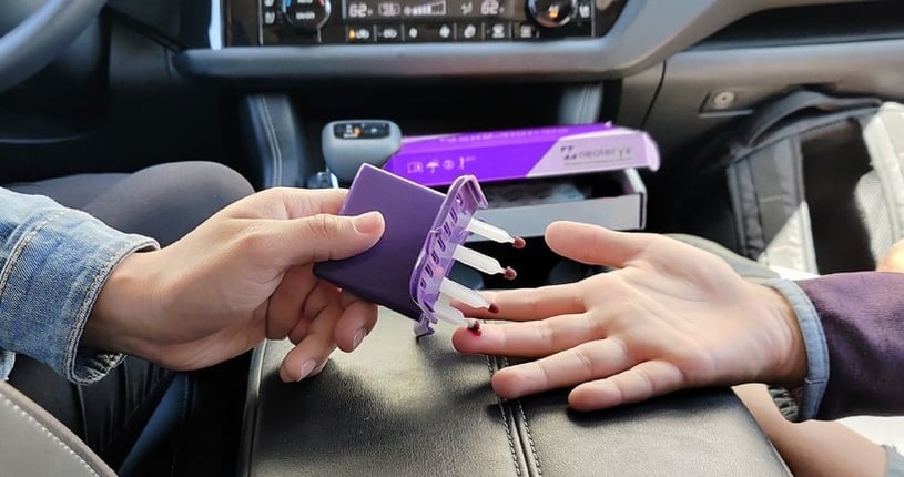 A parent collects a micro blood sample from her child in the car