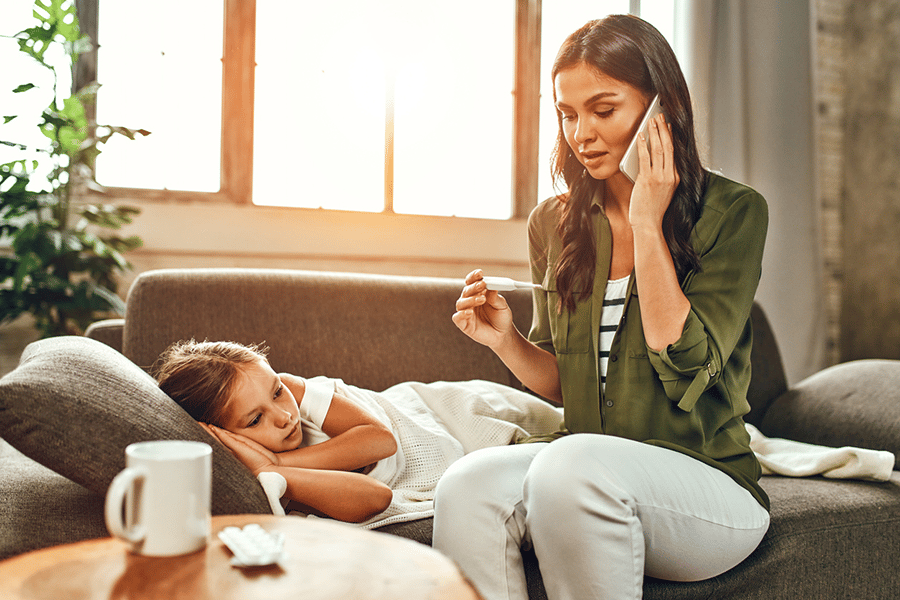 a young girl lies sick on a couch, a worried mother sits next to hear on the phone.