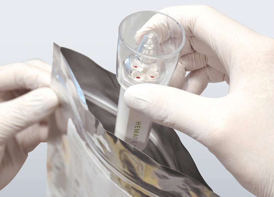 a pair of gloved hands place a tamper proof hemapen device in a collection bag.