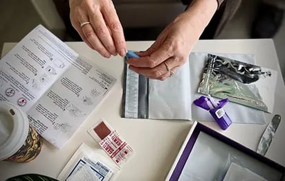 A remote sample collection kit, a hand opens a lancet device