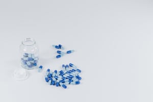 a glass pill bottle half full of pills and several pills are on the table top.