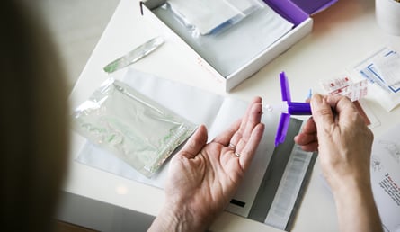 a hand approaches a drop of blood on a finger with a mitra microsampling device