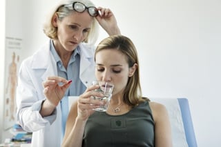 a young women at a clinic sips on a cup of water, a clinical trial facilitator stands in the background