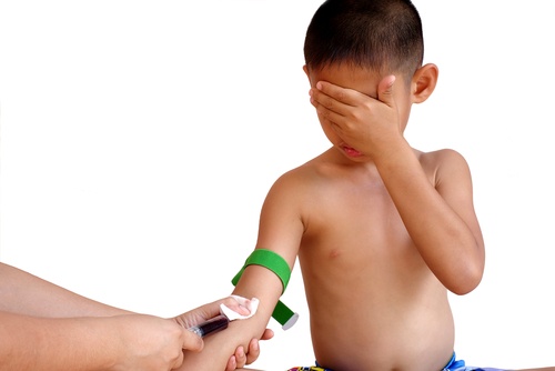 A young boy covers his eyes in fear as a phlebotomist takes a venipuncture blood sample from his arm