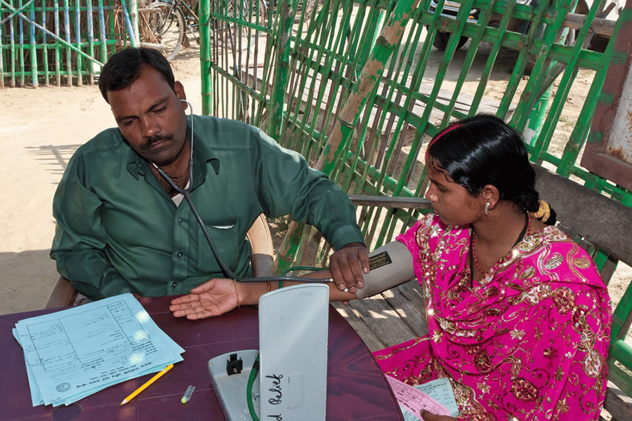 a doctor takes a young womens blood pressure in a remote outdoor setting.