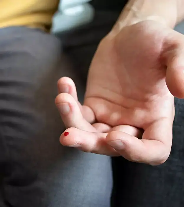 An extended hand with a drop of blood on the middle finger