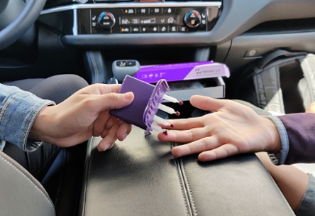 A parent collects a capillary bllod sample from their child in a car